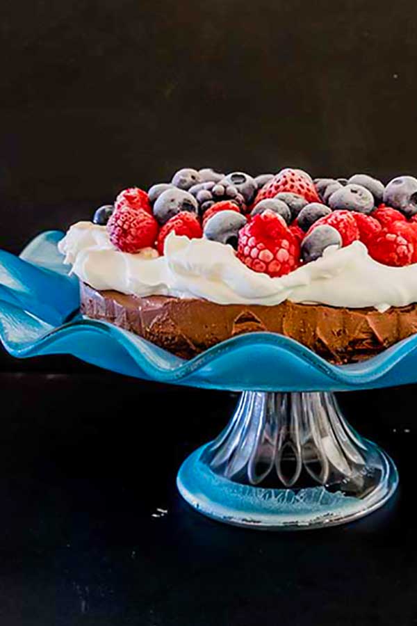 french chocolate silk cake topped with cream and berries on a cake platter