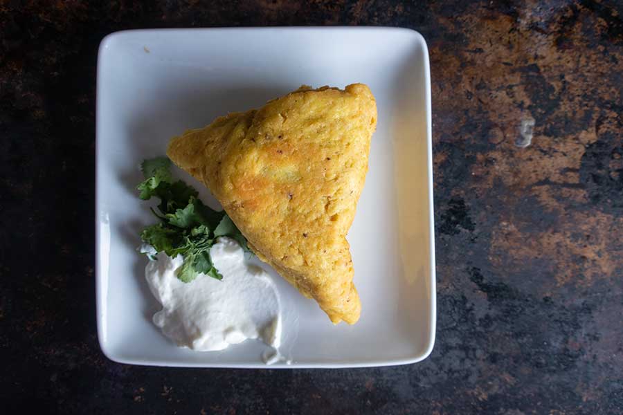 fried gluten-free samosa on a plate with yogurt and cilantro