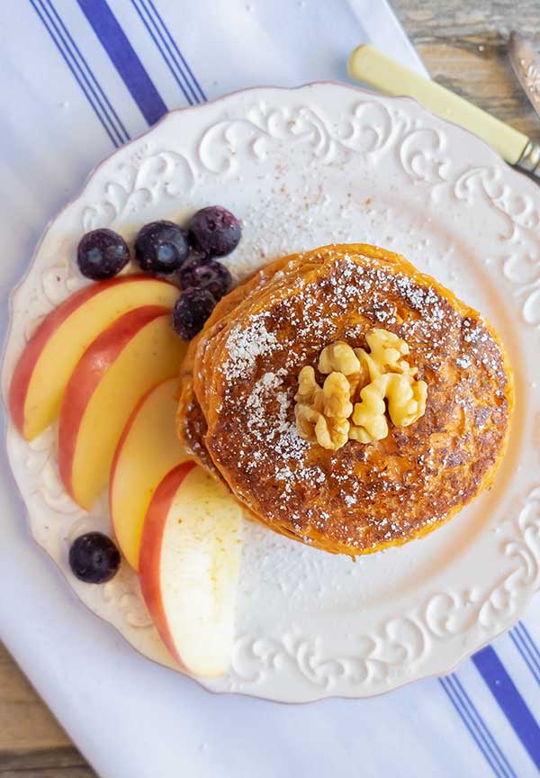 carrot pancakes stacked on a plate with apple sices and blueberries