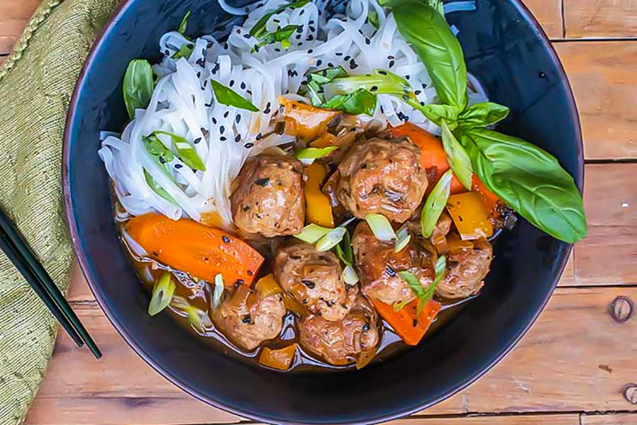 sweet and sour meatballs with sesame rice noodles in a bowl