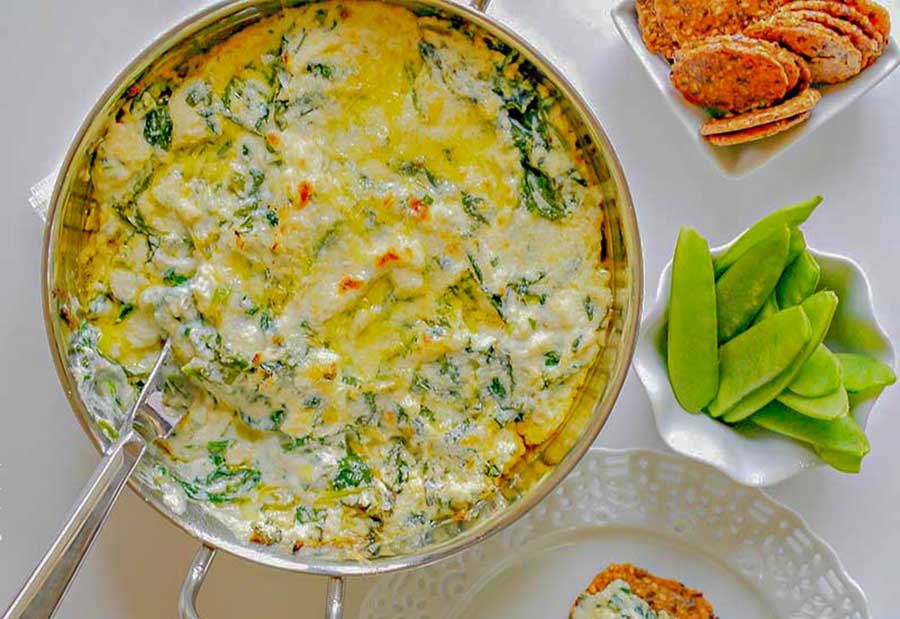 baked spinach ricotta dip in a bowl with crackers and snow peas